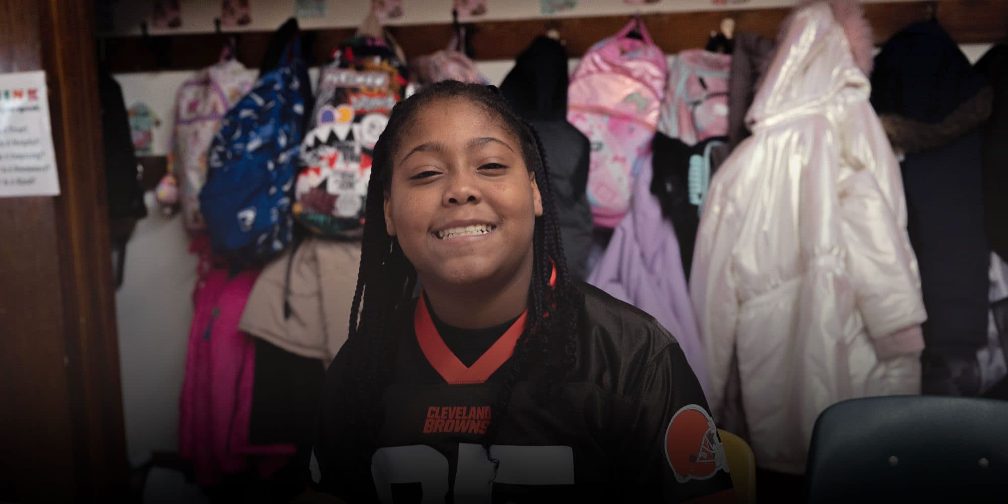 Smiling student in front of classroom coat hooks.