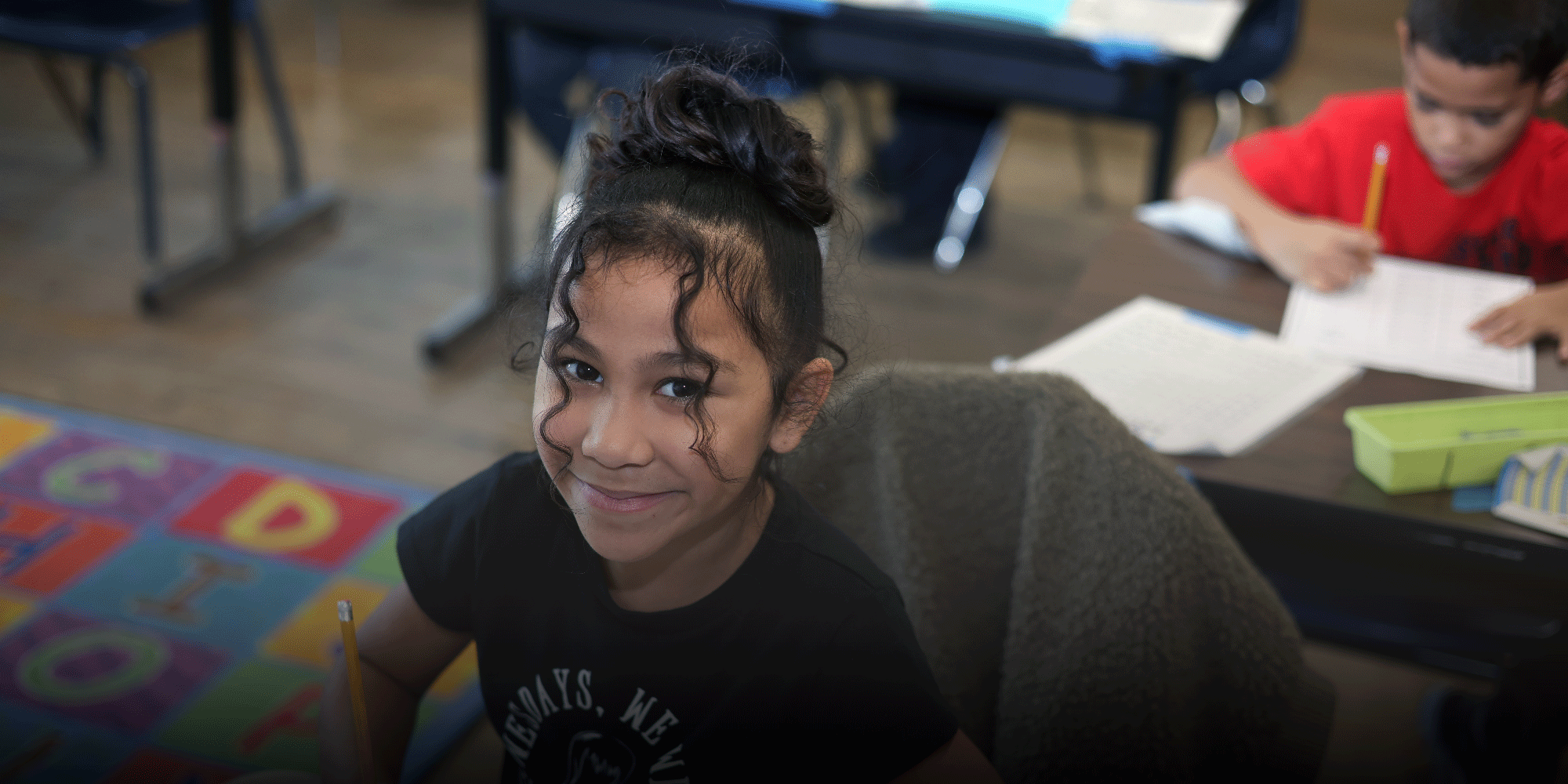 Smiling student holding a pencil in a classroom.