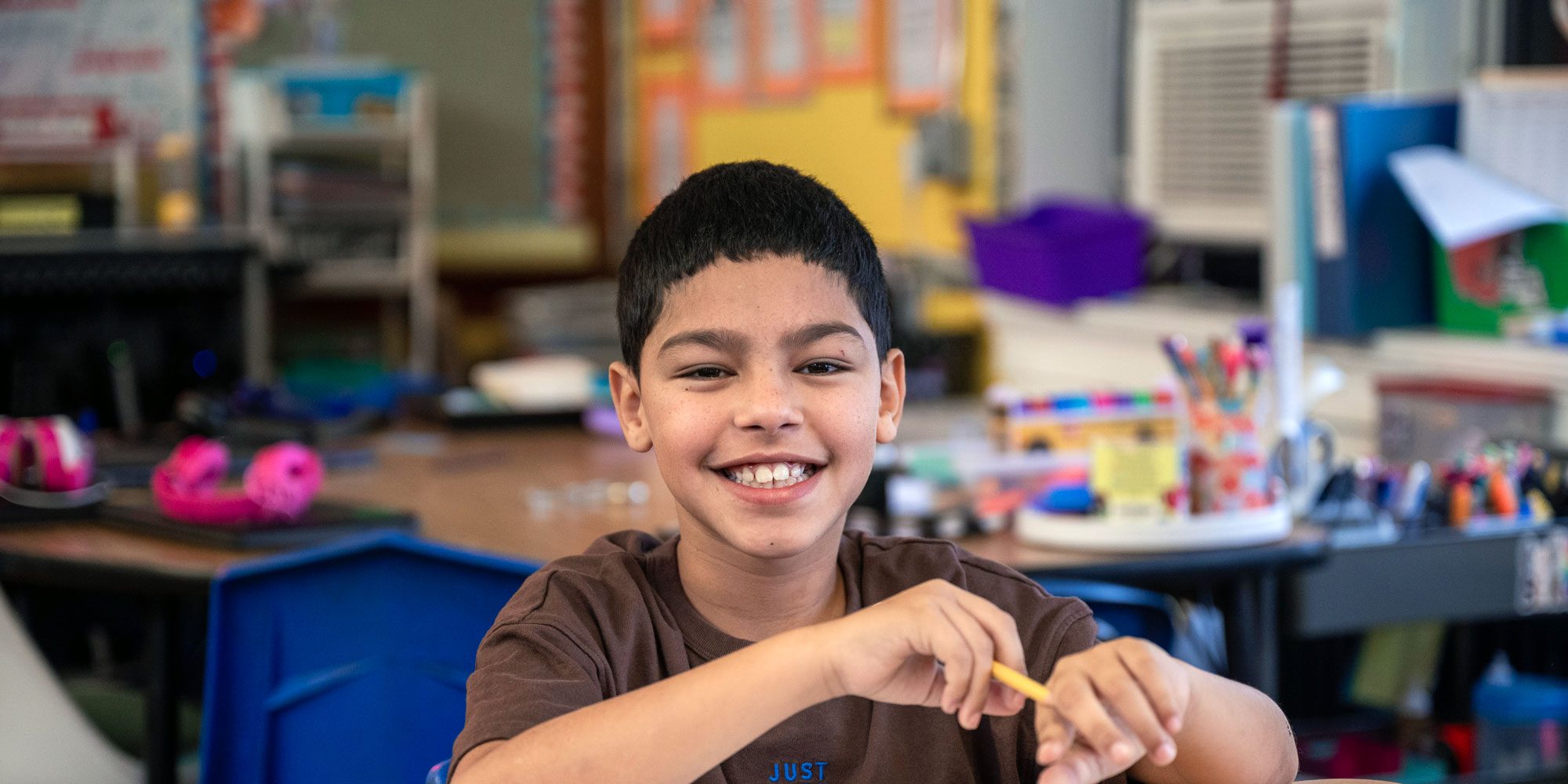 Smiling student holding a pencil at a classroom desk.