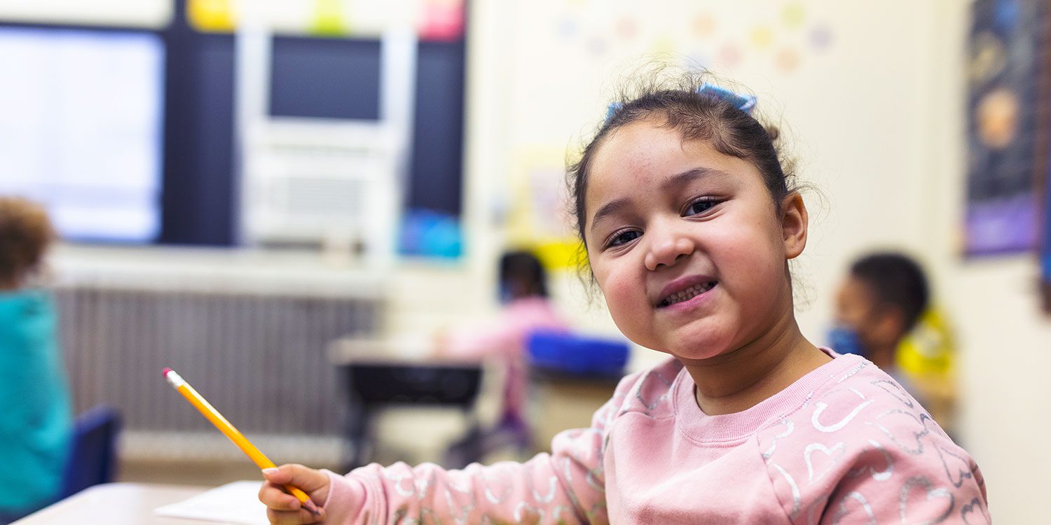 Smiling student writing with a pencil at their desk.